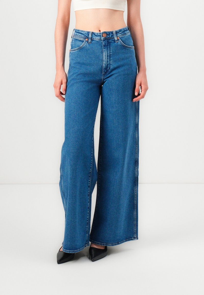 Wide-leg jeans in medium blue denim. Features a high waist, front pockets, and a button closure. Smooth texture with minimal stitching details.