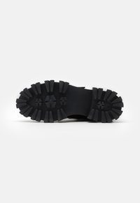 Semelle de chaussure en caoutchouc noir avec des motifs de rainures profonds et angulaires, et un profil large pour une meilleure traction et stabilité. Surface texturée pour l'adhérence.
