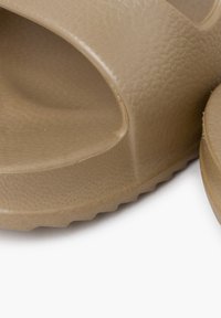 Sandali in plastica beige a scivolo con superficie textured, punta aperta e design curvo. Presentano una suola durevole e rigidas per una buona aderenza.