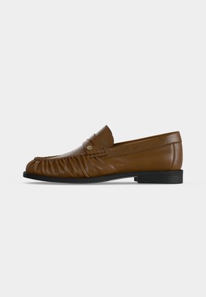 Brun læderloafer med rynkede detaljer foran, sort sål og lille metallogofar på siden, vist fra ydersiden.