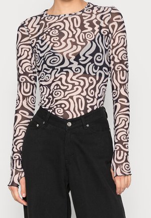 Gennemsigtig bluse med lange ærmer med sorte og beige abstrakte swirl-mønstre kombineret med højtaljede sorte bukser.