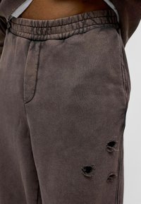 Bruine sweatpants van katoen met een trekkoord in de taille en twee versleten gaten op de dij voor een versleten uitstraling.