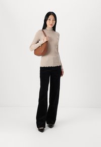 Haut à manches longues en jersey beige, avec un col festonné, associé à un pantalon noir à jambes larges et un sac à bandoulière courbé marron. Chaussures noires à bout pointu.