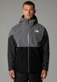 Veste imperméable avec une partie supérieure grise et une partie inférieure noire, dotée d'une fermeture éclair et d'une capuche ajustable. Comprend des poches latérales.