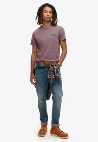 Korte mouw bordeaux heather t-shirt, blauwe jeans, bruine leren laarzen, geruite flanellen stof om de taille geknoopt. Casual fit met opgerolde jeans.
