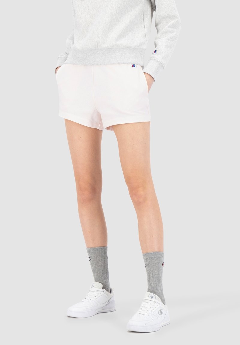 Pantalones cortos rosa claro en un corte relajado, hechos de una tela suave, combinados con un sudadera gris y zapatillas blancas. Calcetines grises con detalles de logo.