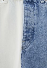 Jeans en denim avec un design divisé, présentant des matériaux bleu clair et blanc, des textures dégradées et des détails de couture contrastés.