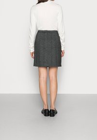 Falda de tweed gris con un diseño recto, que presenta una cintura de altura media y un dobladillo por encima de la rodilla, combinada con zapatos negros y una blusa blanca.