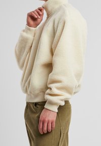 Cremfarbener Pullover aus weichem, strukturiertem Fleece mit hohem Kragen und gerippten Bündchen, kombiniert mit khakifarbenen Cordhosen.