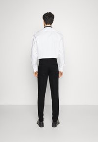 Camicia bianca a maniche lunghe con colletto nero, abbinata a pantaloni neri; tessuto liscio, vestibilità su misura e senza motivi o accessori visibili.