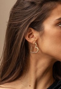 Orecchini a forma di cuore in tonalità oro, con accenti di strass, dalla finitura liscia e lucida e un design geometrico.