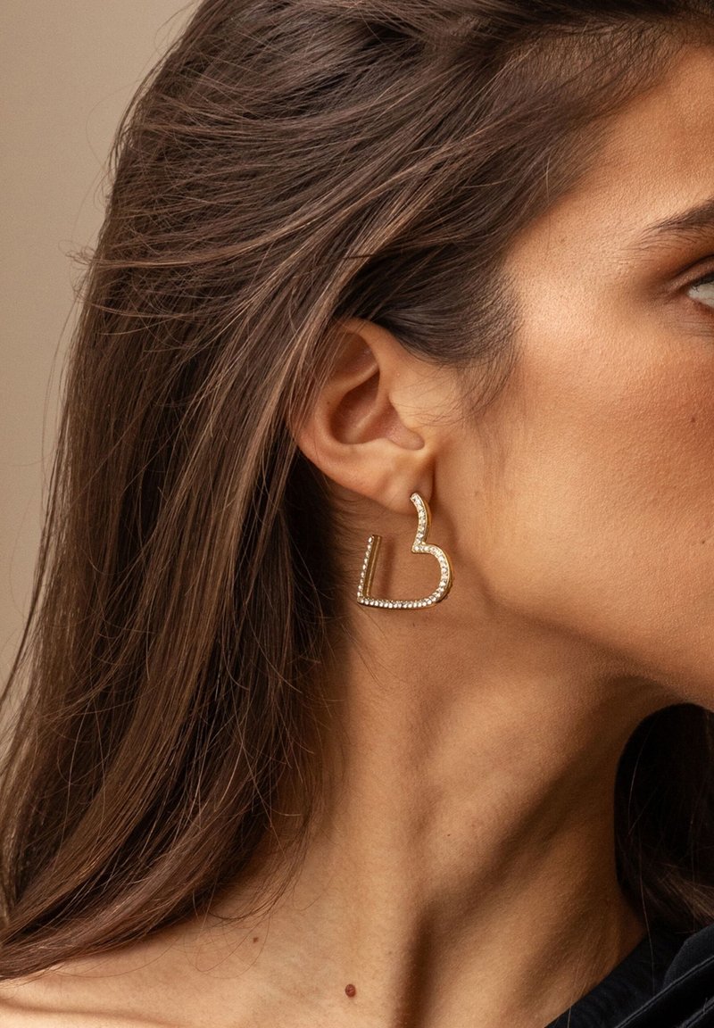 Orecchini a forma di cuore in tonalità oro, con accenti di strass, dalla finitura liscia e lucida e un design geometrico.