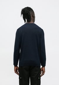 Tumesinist värvi pusakate pehmest kangast, millel on pikad varrukad, soonikuga kaelus ja mansetid, lõdvaistmeline lõige ning minimalistlik disain.