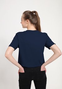 Navy blue short-sleeve t-shirt with a classic fit, round neckline, and smooth texture; worn with black jeans, showing a casual style.