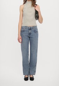 Top a righe senza maniche, jeans a gamba larga blu e ballerine nere. L'outfit presenta una texture in denim e semplici motivi con una silhouette casual.