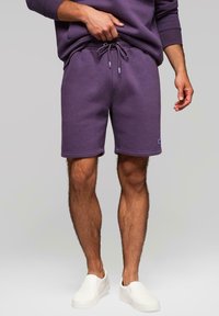 Fialové šortky z bavlněné směsi s volným střihem, elastickým pasem a šňůrkou, a malou logo nášivkou na lemu.