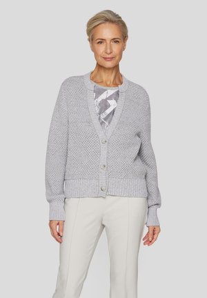 Light grey knitted cardigan with a textured pattern, v-neck, and five buttons. Paired with a light-colored top and pants.