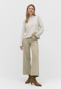 Ljusbeige sweater med hög hals, kombinerad med vida khaki-byxor. Bruna ankelstövlar med spetsiga tår. En enkel och modern design.