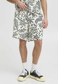 Pantalones cortos crema con estampado botánico en azul marino, cinturilla elástica, bolsillos laterales y un corte holgado, combinados con zapatillas negras y calcetines blancos.