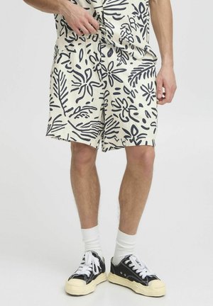 Shorts en crème avec un imprimé botanique marine, taille élastique, poches latérales et coupe ample, associés à des baskets noires et des chaussettes blanches.