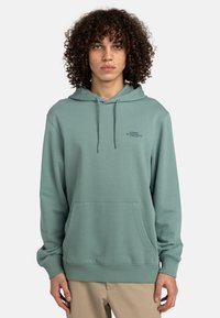 Sudadera verde de tejido suave con un bolsillo frontal, puños acanalados y capucha ajustable con cordón. Presenta un pequeño logo en el pecho.