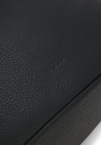 Surface en cuir noir texturé avec le mot "BOSS" subtilement embossé au centre.