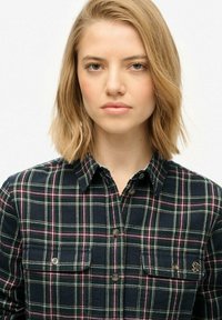 Navy plaid shirt featuring green, white, and pink lines, two chest pockets, button-up front, and a branded accent above the left pocket.