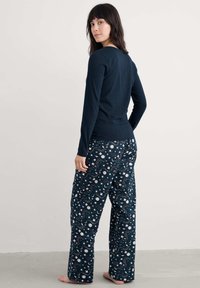 Námořnický dlouhý rukáv vrchní část spojená s kalhotami na stahování s potiskem, které obsahují nebeské vzory v zelené a bílé na tmavém pozadí.