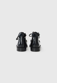 Schwarze Ankle-Boots aus glänzendem Leder, mit runder Zehenpartie, Rückenschnürung und einer dicken schwarzen Sohle mit dekorativem Stichdetail.
