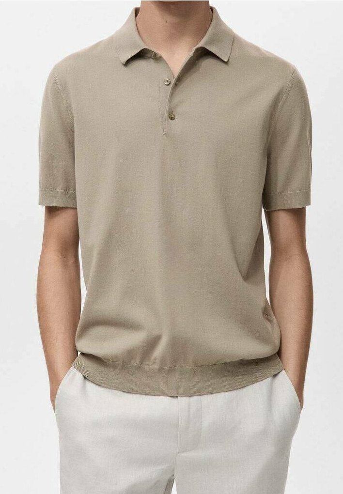 Homme portant un polo beige à manches courtes légèrement rentré dans un pantalon clair, les mains dans les poches.