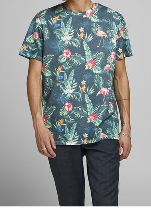 Mężczyzna noszący krótkim rękawem granatowy T-shirt z kolorowymi tropikalnymi kwiatowymi i flamingowymi wzorami, w połączeniu z ciemnymi spodniami.