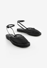 Svarta flätade sandaler med en strukturerad överdel, ankelrem och platt sula. Har en dekorativ pärldesign och rund tå.