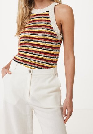 Gebreide tanktop met meerkleurige strepen (geel, rood, zwart) en een beige halslijn. Gecombineerd met witte high-waisted broek.