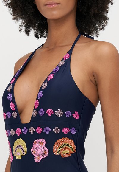 Tengerészi, nyakban megkötős fürdőruha, élénk, hímzett kagylómotívumokkal rózsaszín, lila és arany színekben. Mély V-nyakú kialakítás, sima textúrával.