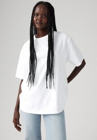T-shirt blanche à manches courtes, coupe ample, col rond, associée à un jean bleu clair. Tissu en coton doux, design minimaliste.