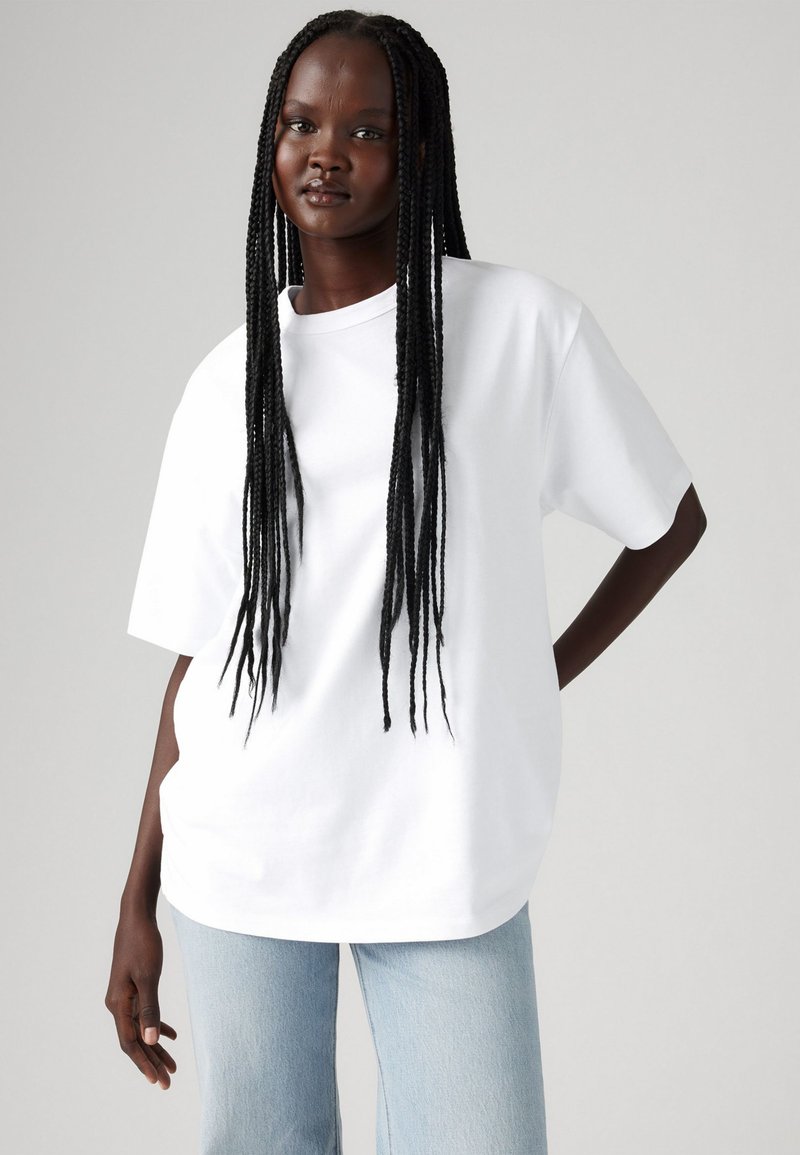 T-shirt blanche à manches courtes, coupe ample, col rond, associée à un jean bleu clair. Tissu en coton doux, design minimaliste.