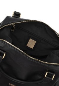 Svart läderhandväska med dragkedja. Invändig har den en accent i guldton, svart tygfoder och en liten etikett.