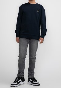 Sweat-shirt bleu marine avec un col rond et un petit patch logo. Porté avec un jean gris et des baskets noir et blanc. Design simple.