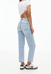 Vaqueros de tiro alto en azul claro con detalles desgastados, diseño de pierna recta y cinco bolsillos, combinados con zapatillas blancas y una camiseta blanca.