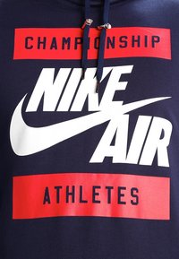Mörkblå sweatshirt med en stor vit Nike-logotyp, röd text som säger "CHAMPIONSHIP" och "ATHLETES", med dragsnören och en mjuk tygkänsla.