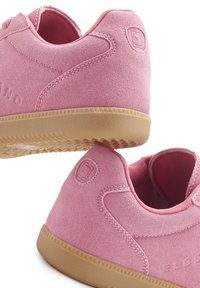 Pink suede sneakers with a smooth texture, round shape, and rubber gum sole. Features minimal stitching and a logo on the heel.