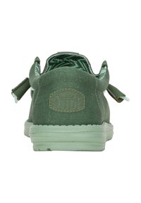 Zapatillas deportivas de lona verde con tejido texturizado, suela de goma y un bucle para ponerse fácilmente. Cuenta con un ligero tacón y un forro interior con patrón.
