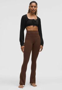 Czarny krótkie sweter z detalem w postaci wiązania, zestawiony z brązowymi spodniami z wysokim stanem i szerokimi nogawkami. Gładka tekstura, dopasowany fason i minimalistyczny styl.