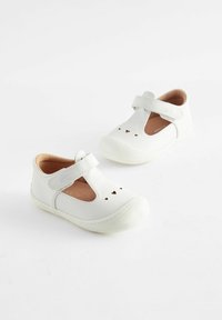 Valkoiset nahkakengät, joissa on T-nauhalta muotoiltu design, suljettu kärki ja sydänleikkauksia. Varustettu pintakuvioidulla kumipohjalla ja pehmeällä sisusvuorella.