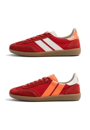 Deux baskets basses rouges avec semelles en gomme, l'une avec des bandes blanches et un onglet au talon, l'autre avec des bandes orange et un onglet au talon, vues de côté.