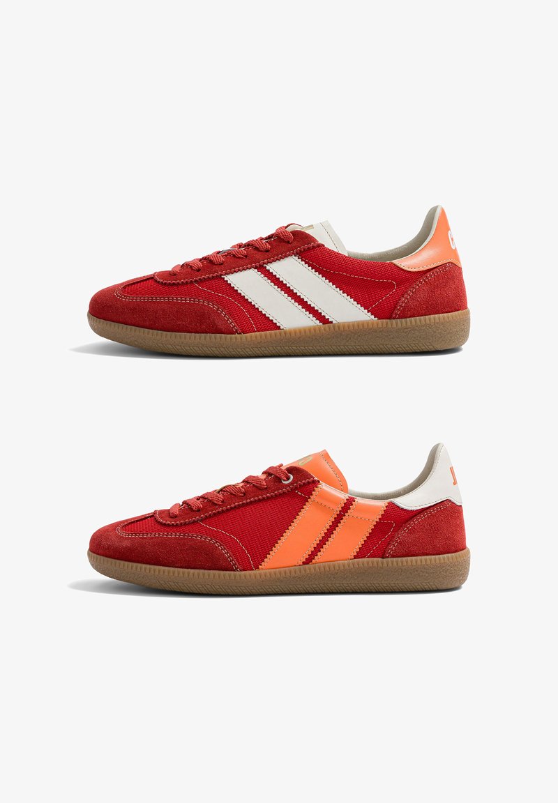 Deux baskets basses rouges avec semelles en gomme, l'une avec des bandes blanches et un onglet au talon, l'autre avec des bandes orange et un onglet au talon, vues de côté.