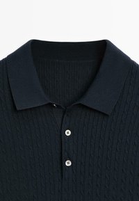 Polo shirt navy in maglia con texture a coste, dotato di colletto e chiusura a tre bottoni, realizzato in materiale morbido e elastico.