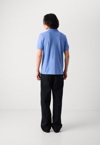 Cămașă polo de culoare albastru deschis cu guler, mâneci scurte, fisuri laterale, asortată cu pantaloni negri înceți. Textura materialului este moale, fără modele vizibile.