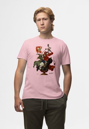 Roze T-shirt met een grafische bloembakken in levendig rood, wit en blauw, met een zwart versierde vaas en een verguld voetstuk.