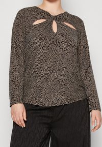 Top a maniche lunghe con stampa animale, caratterizzato da un dettaglio a chiave sul colletto. I colori includono nero e cammello, realizzato in un tessuto morbido e testurizzato.